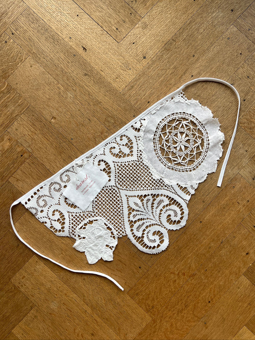 White lace belt scarf with a circular mandala design and delicate floral lace details, laid flat on a wooden floor.