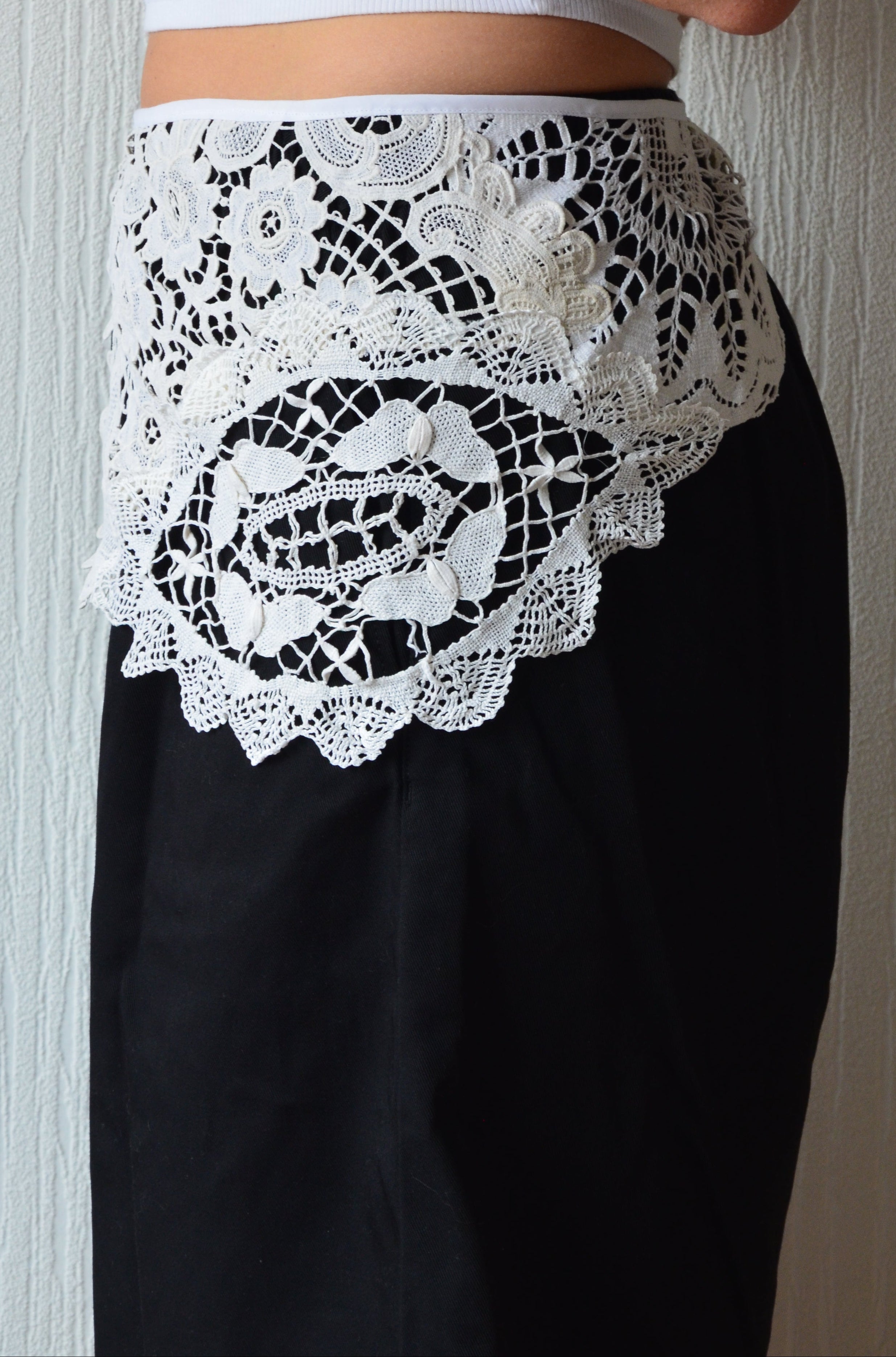 A close-up of a person wearing black shorts with a wide white lace overlay at the hem, paired with a white top. 