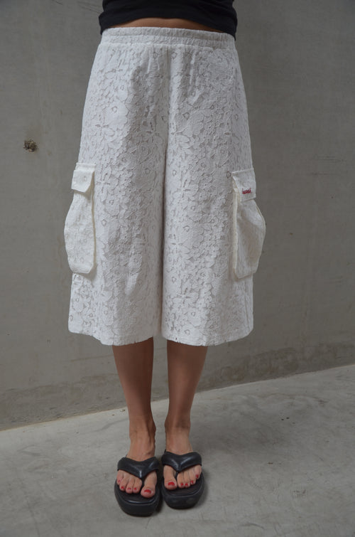 Person wearing white lace shorts and black sandals on a concrete floor.