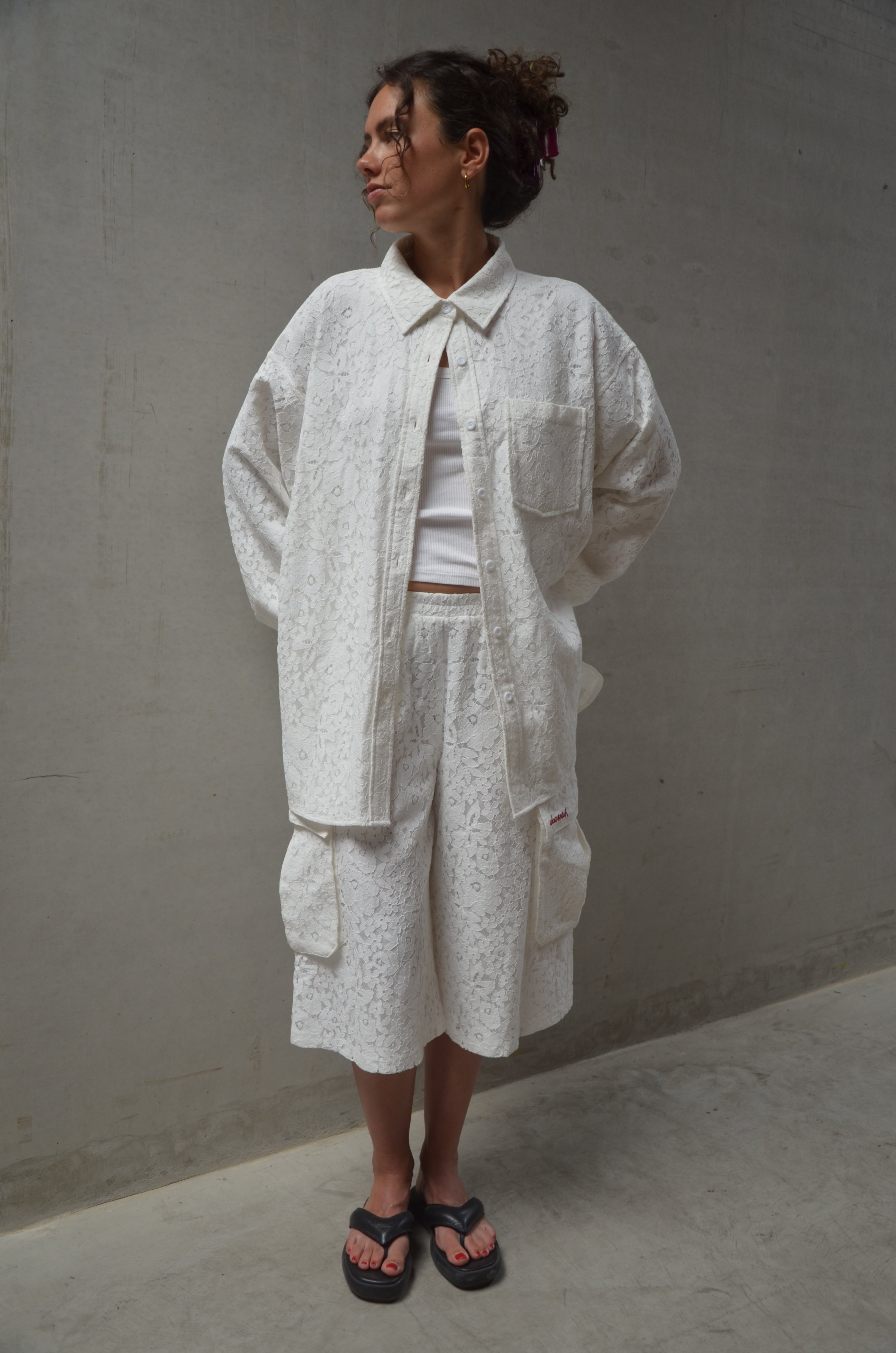 Person wearing a light-colored lace outfit standing against a plain background