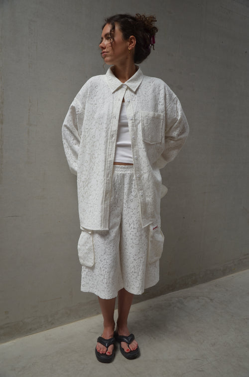 Person wearing a light-colored lace outfit standing against a plain background
