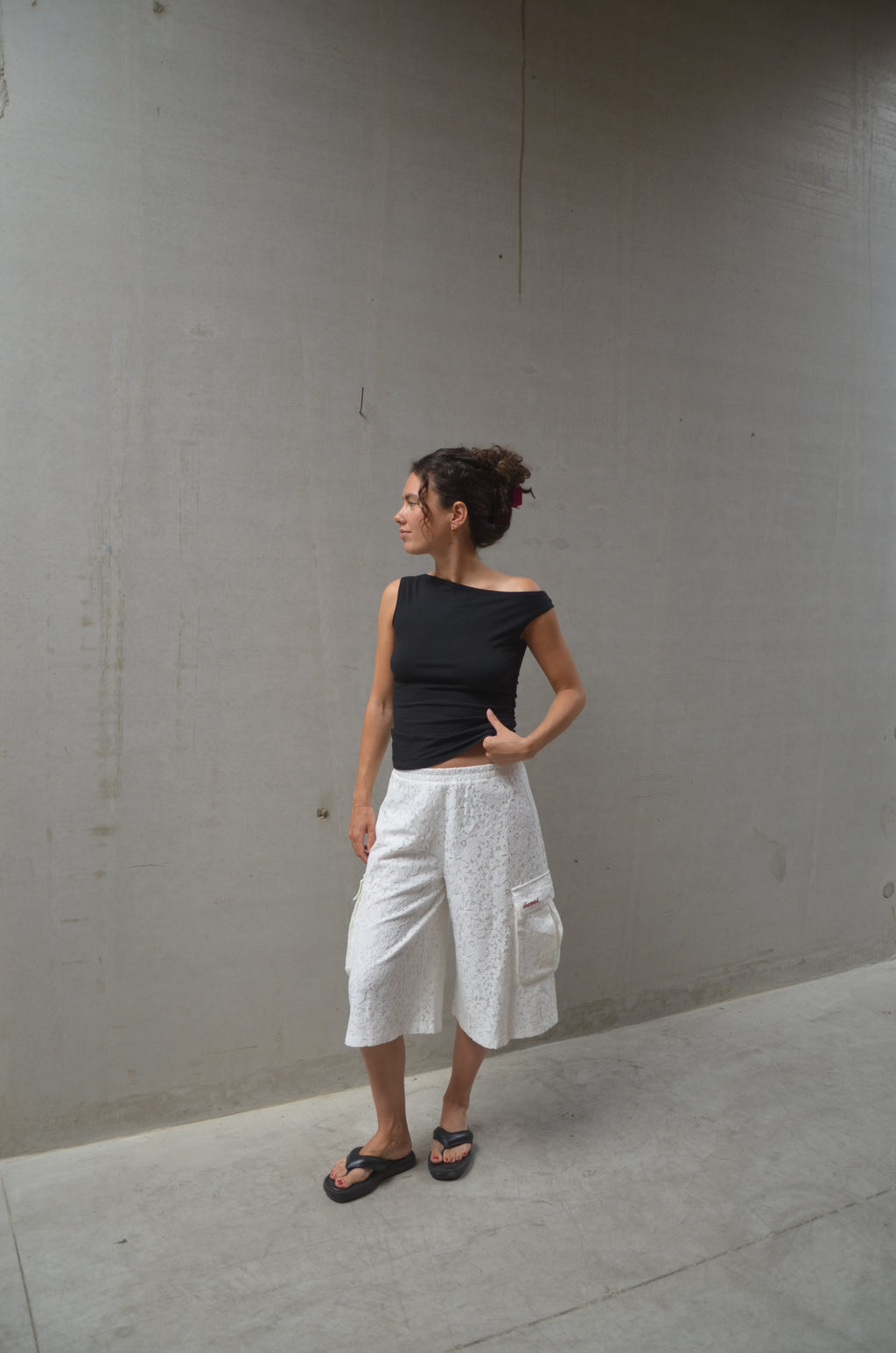 Person wearing a black top and white lace shorts standing on a concrete floor.